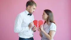 Pár drží poloviny rozbitého srdce na růžovém pozadí, symbol rozchodu
