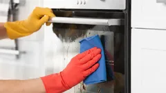 Čištění trouby houbičkou, ruce v gumových rukavicích, úklid domácnosti.