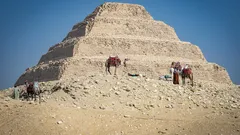 Velbloudi před stupňovitou pyramidou Djosera v egyptské poušti Saqqara