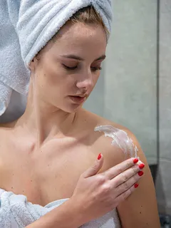 žena s turbanem nanáší tělový krém na rameno