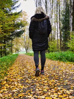 Žena kráčí podzimní cestou pokrytou listím