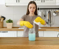 Žena v rukavicích připravuje čisticí prostředek v kuchyni, domácí úklid a hygiena.