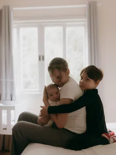 Matka objímá své děti na posteli v domácím prostředí